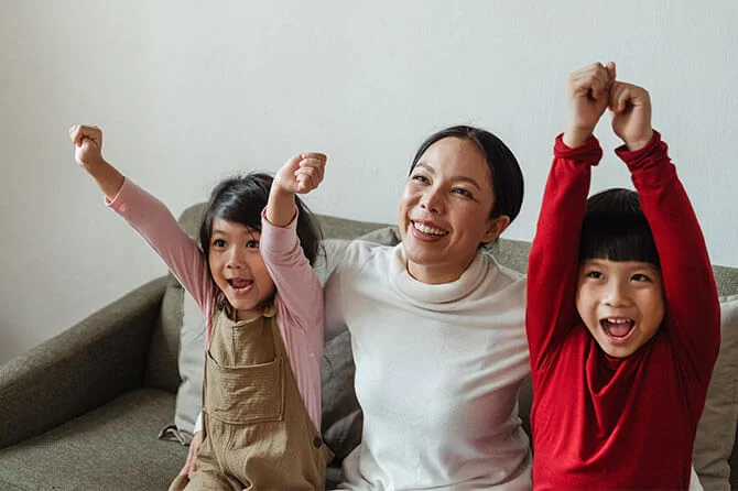 Children and parent excitedly watching TV on a sofa