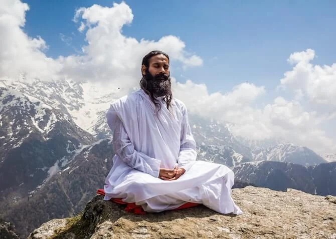 indian man wearing white meditating on a mountain