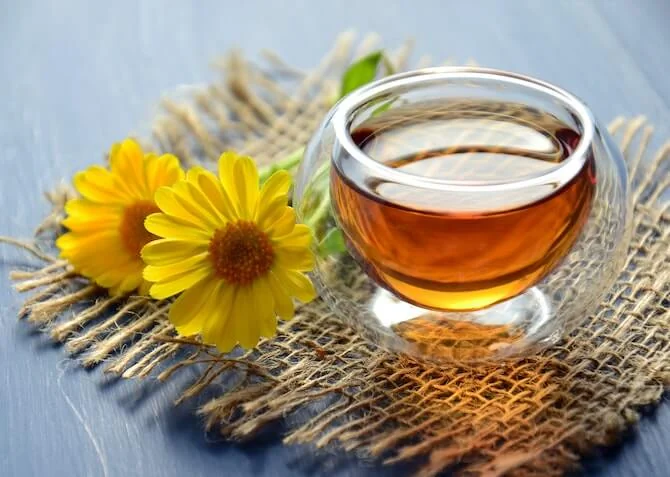 a tea in a strange glass with some flowers resting beside it