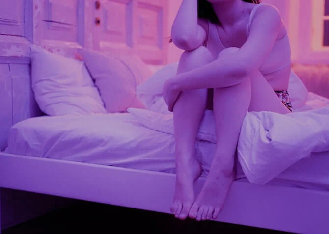 woman sitting in bedroom with pink lighting struggling to sleep
