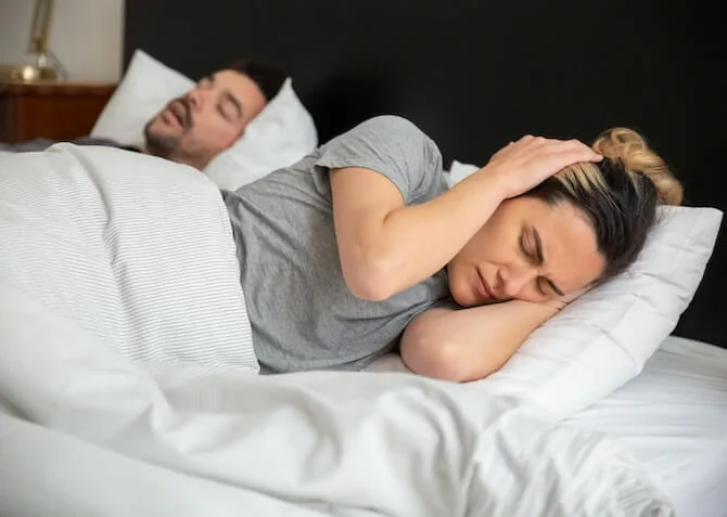 woman covering her ears in frustration at her snoring husband