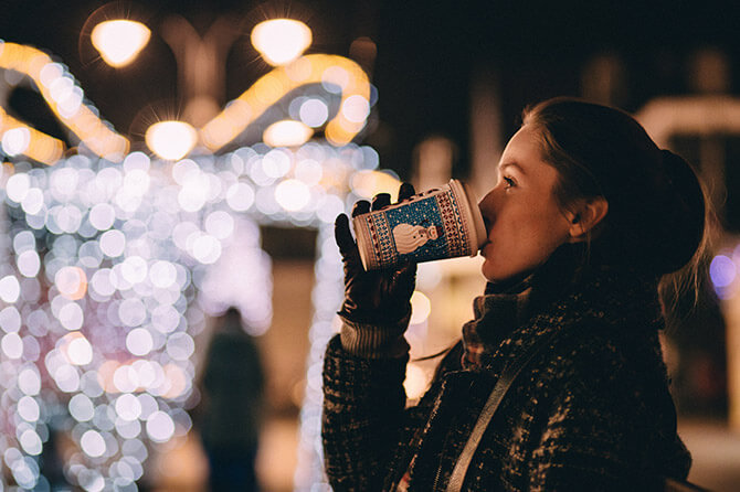 A woman drinks a beverage a street decorated for Christmas