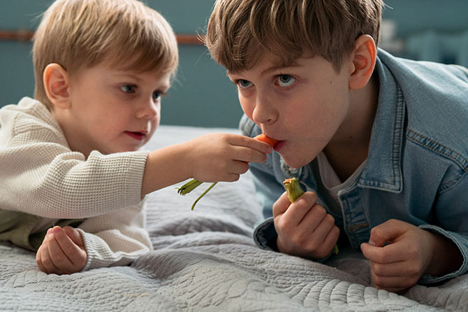 Two boys eating snacks on a bed