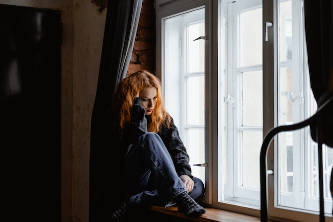 Exhausted woman sitting on window ledge