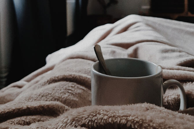 Steaming cup of tea resting on a beige duvet