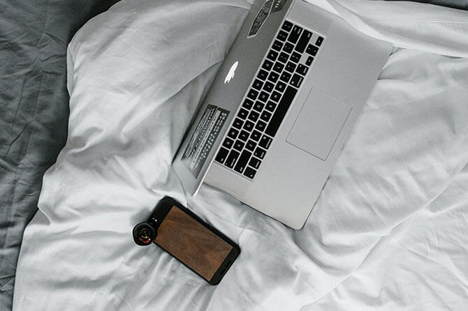 A laptop and a mobile phone resting on an unmade bed