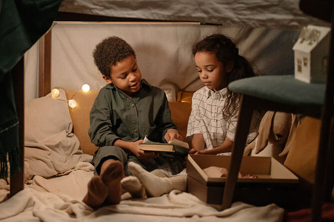 Children in a den made under a table with blankets and pillows