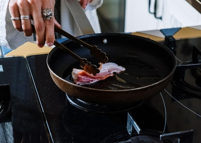 Woman cooking bacon in a pan in the kitchen