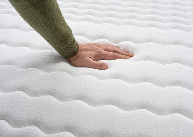 a hand softly pressing down onto a quilted mattress