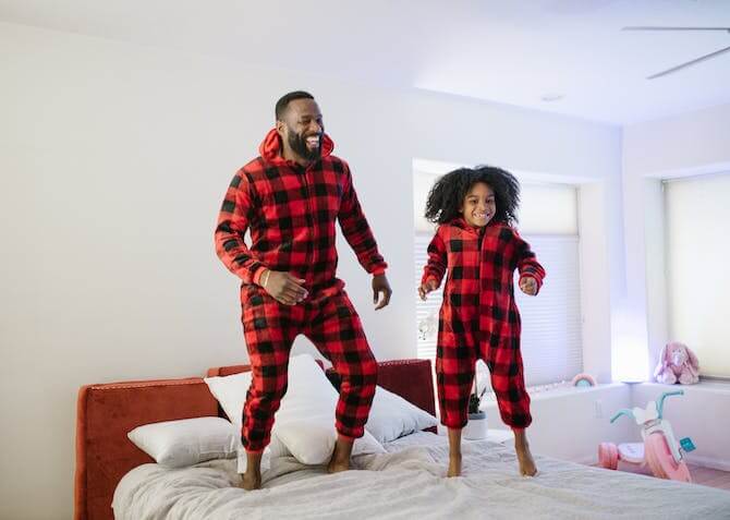 dad and daughter jumping on bed in matching pyjamas