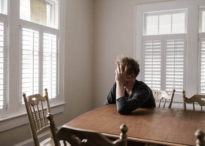 man sitting at a dining table with his head in his hand feeling stressed