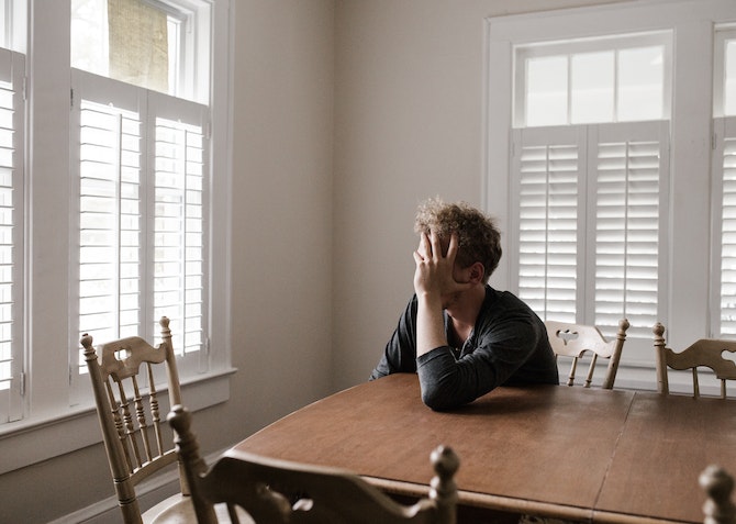 tired and stressed man sitting at a kitchen table with head in hands