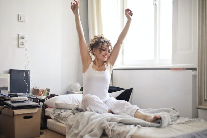 woman smiling and stretching on a bed in the morning light